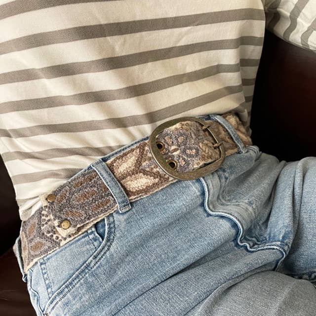 Person wearing a patterned belt and jeans.