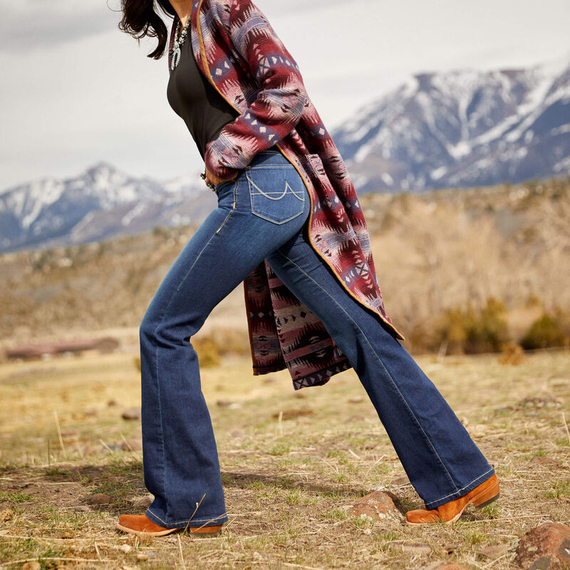 Woman in jeans and patterned coat, mountains in background.