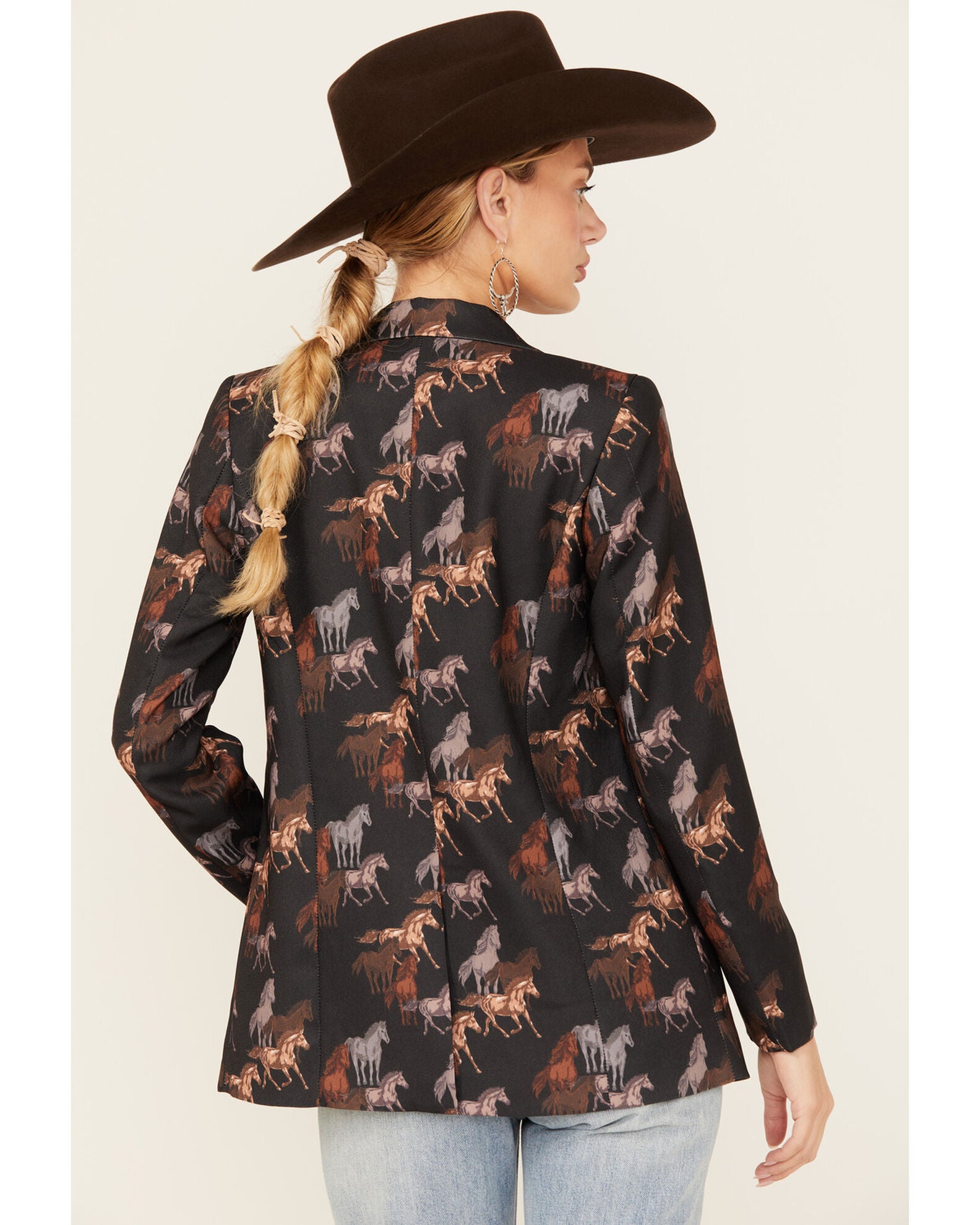 Woman in a black blazer with horse print, wearing a cowboy hat.