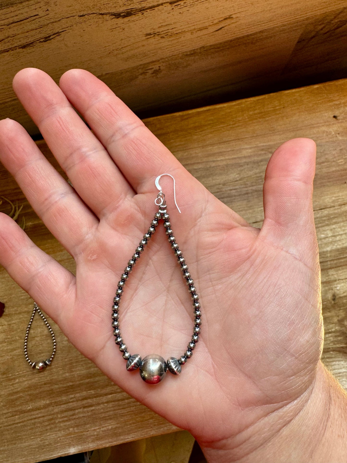 Hand holding sterling silver beaded teardrop earrings.