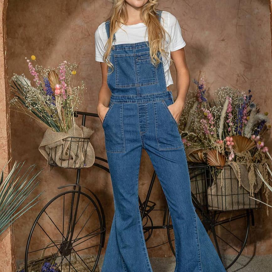 Woman in denim overalls standing by a bicycle.