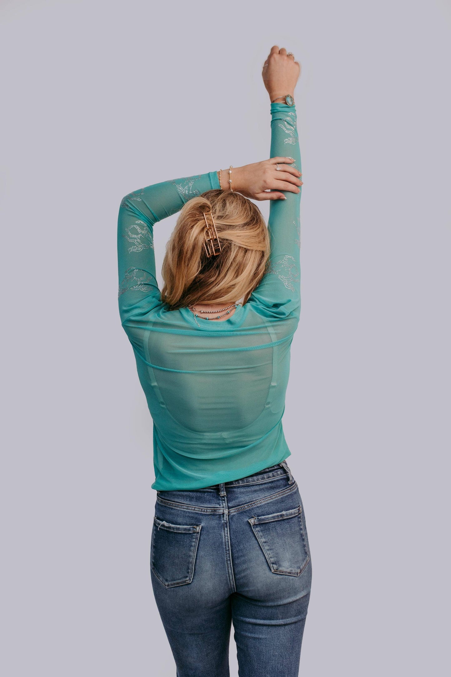 Woman in teal shirt and jeans, arms raised.