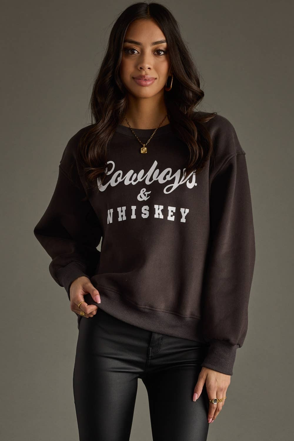 Woman wearing a brown Cowboys & Whiskey sweatshirt and black pants.
