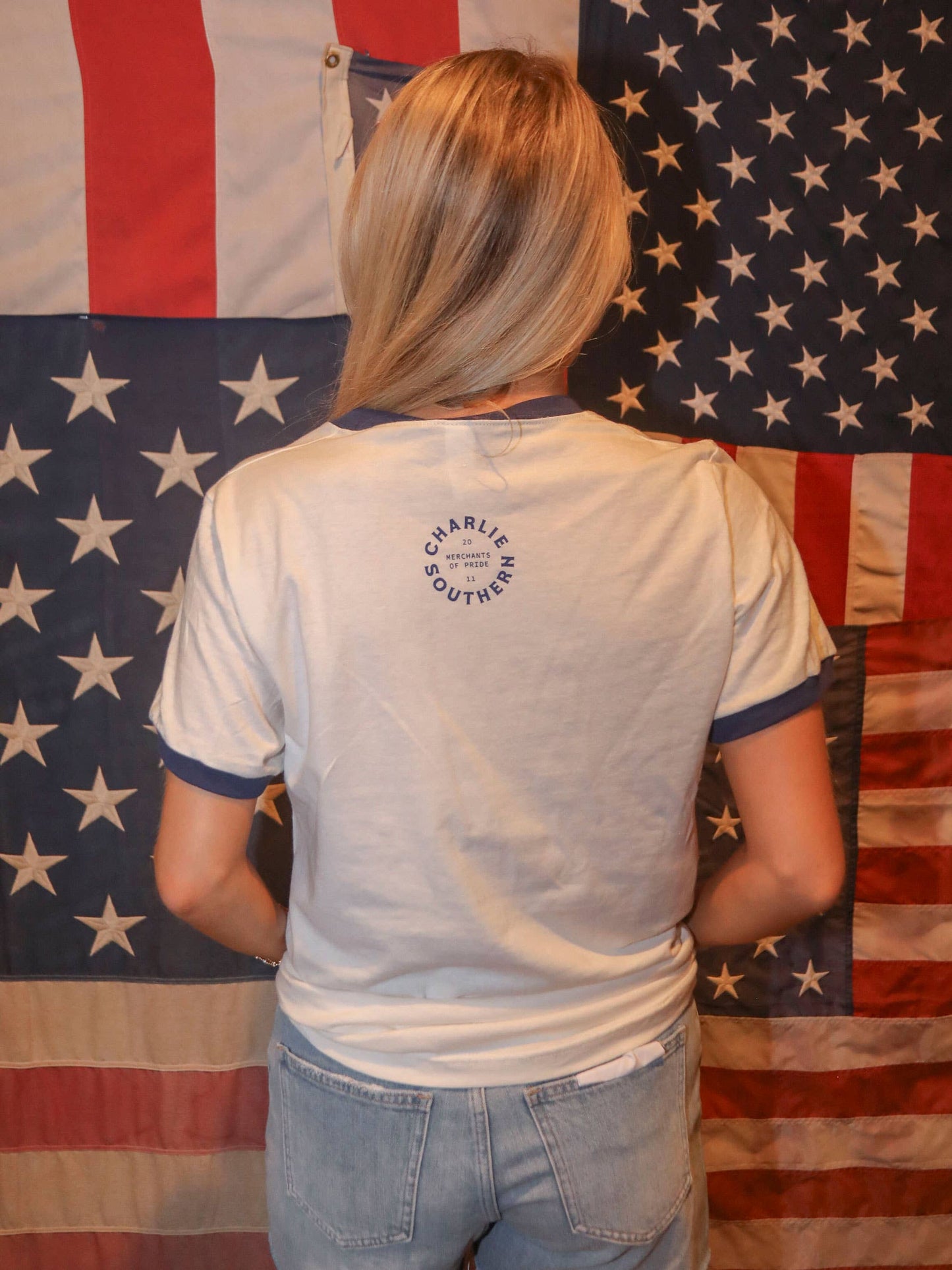 Woman in white shirt with blue trim, standing in front of American flags.