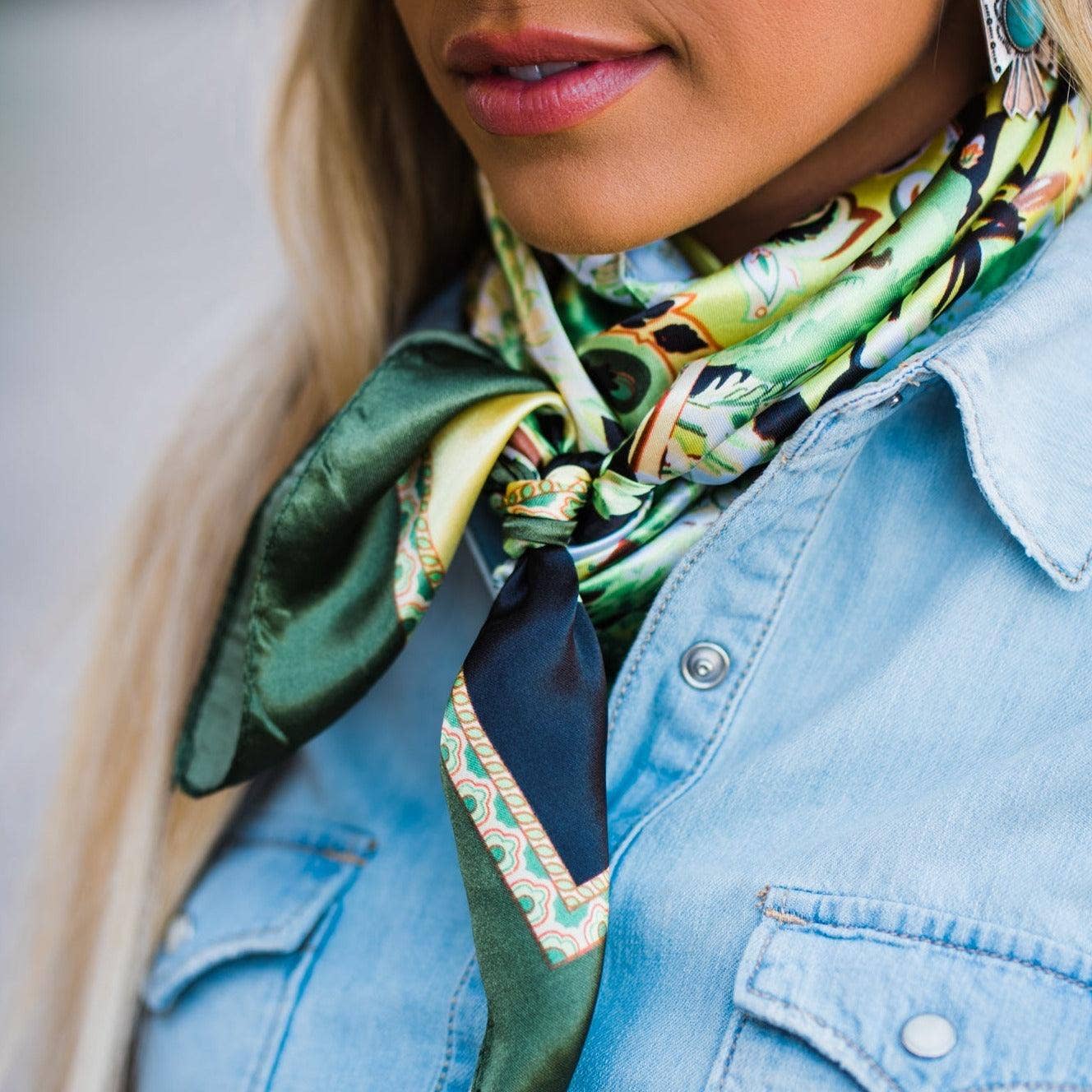 Woman wearing a green patterned scarf and denim shirt.