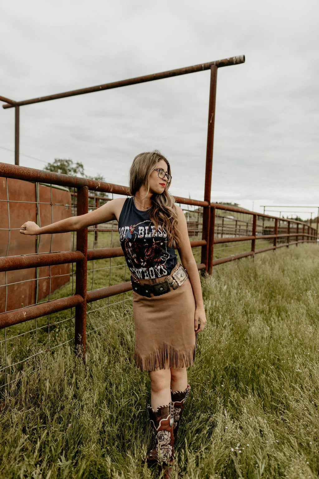 Cowgirl in fringe skirt leans on fence, 8L5A9519