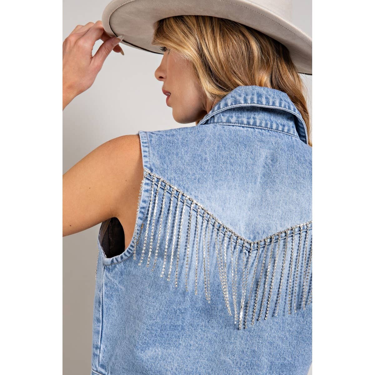 Woman wearing a denim vest with fringe, holding a hat.
