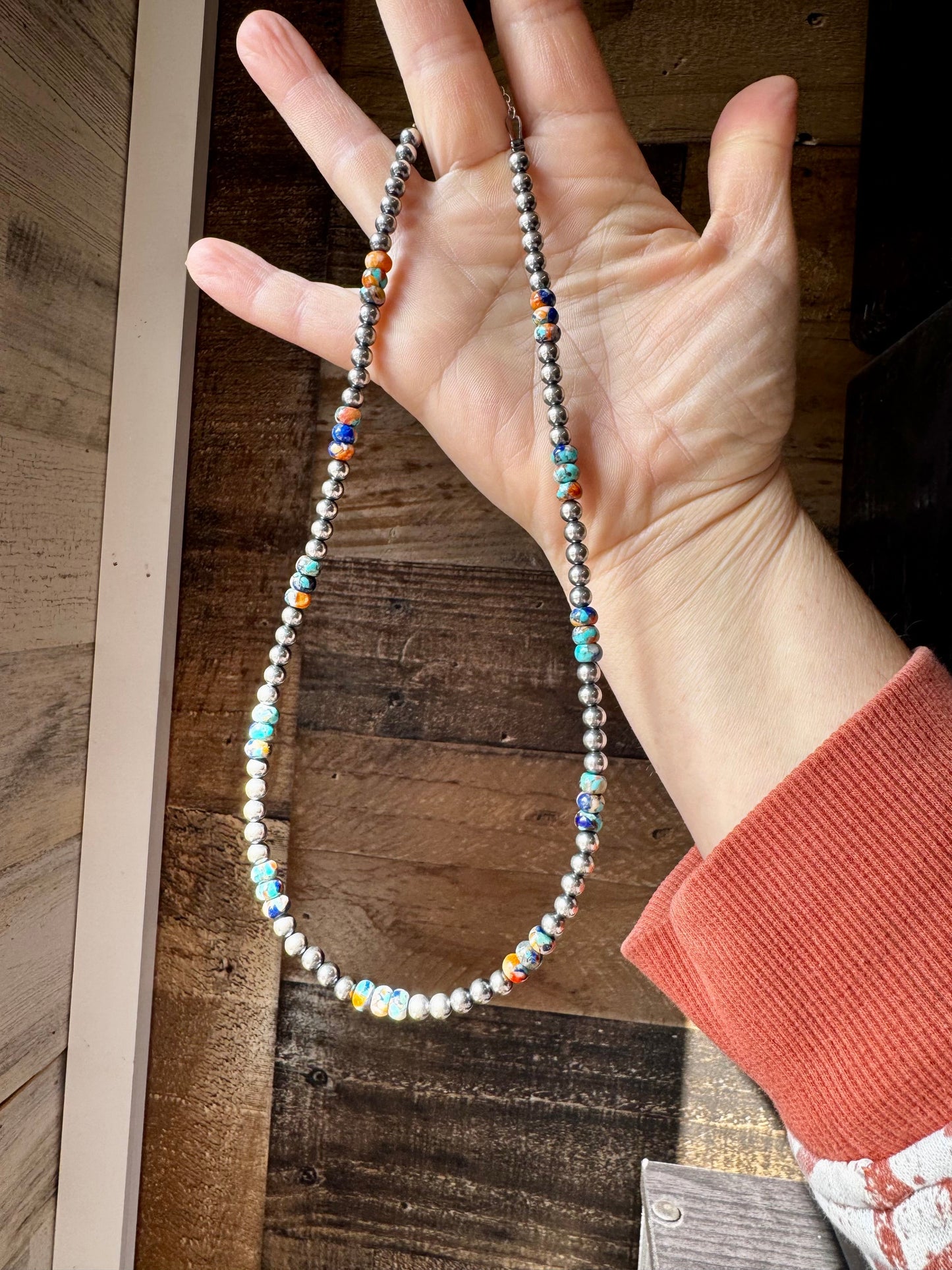 Turquoise & silver beaded necklace held in hand.