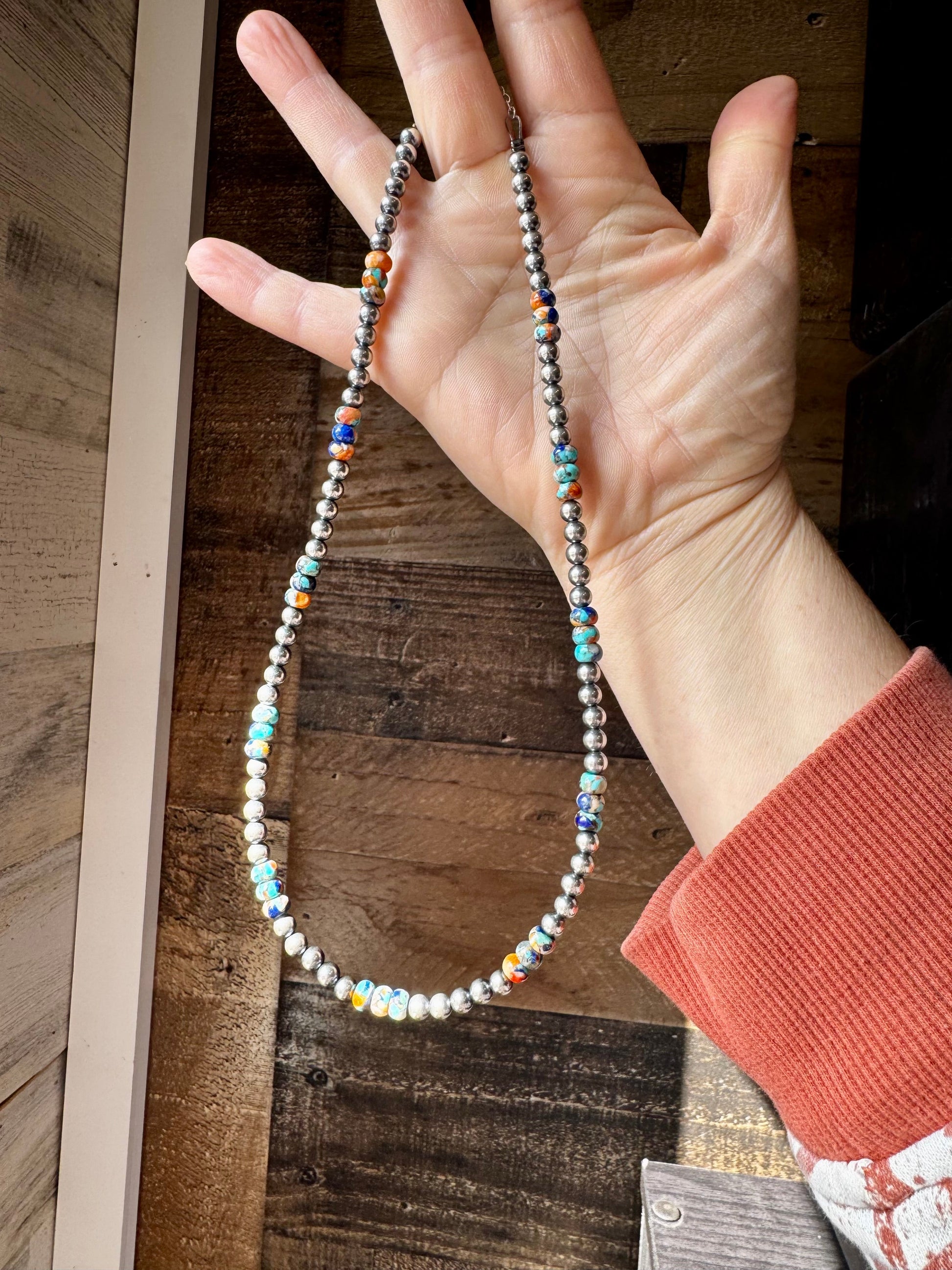 Turquoise & silver beaded necklace held in hand.