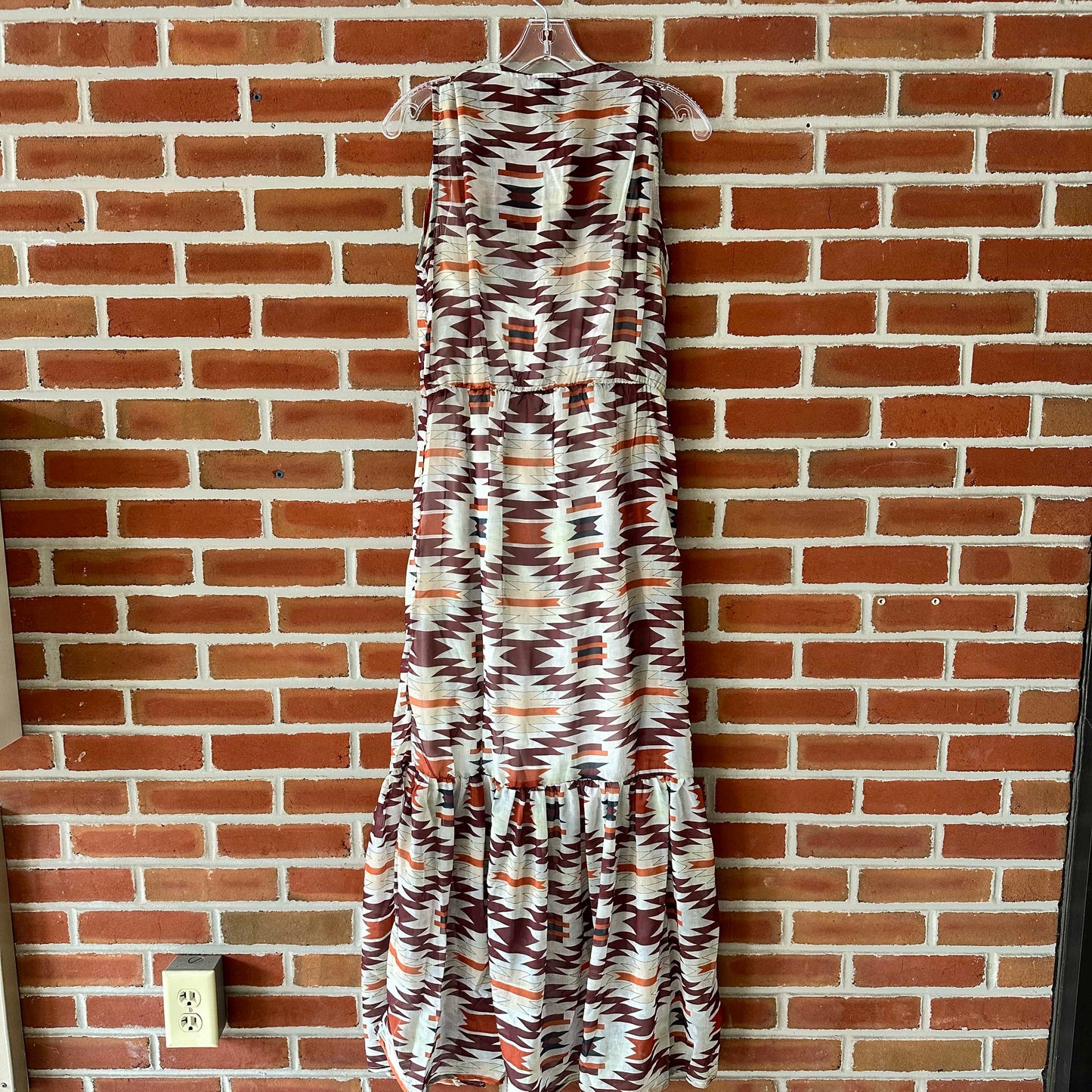 Sleeveless patterned dress hanging on a brick wall.