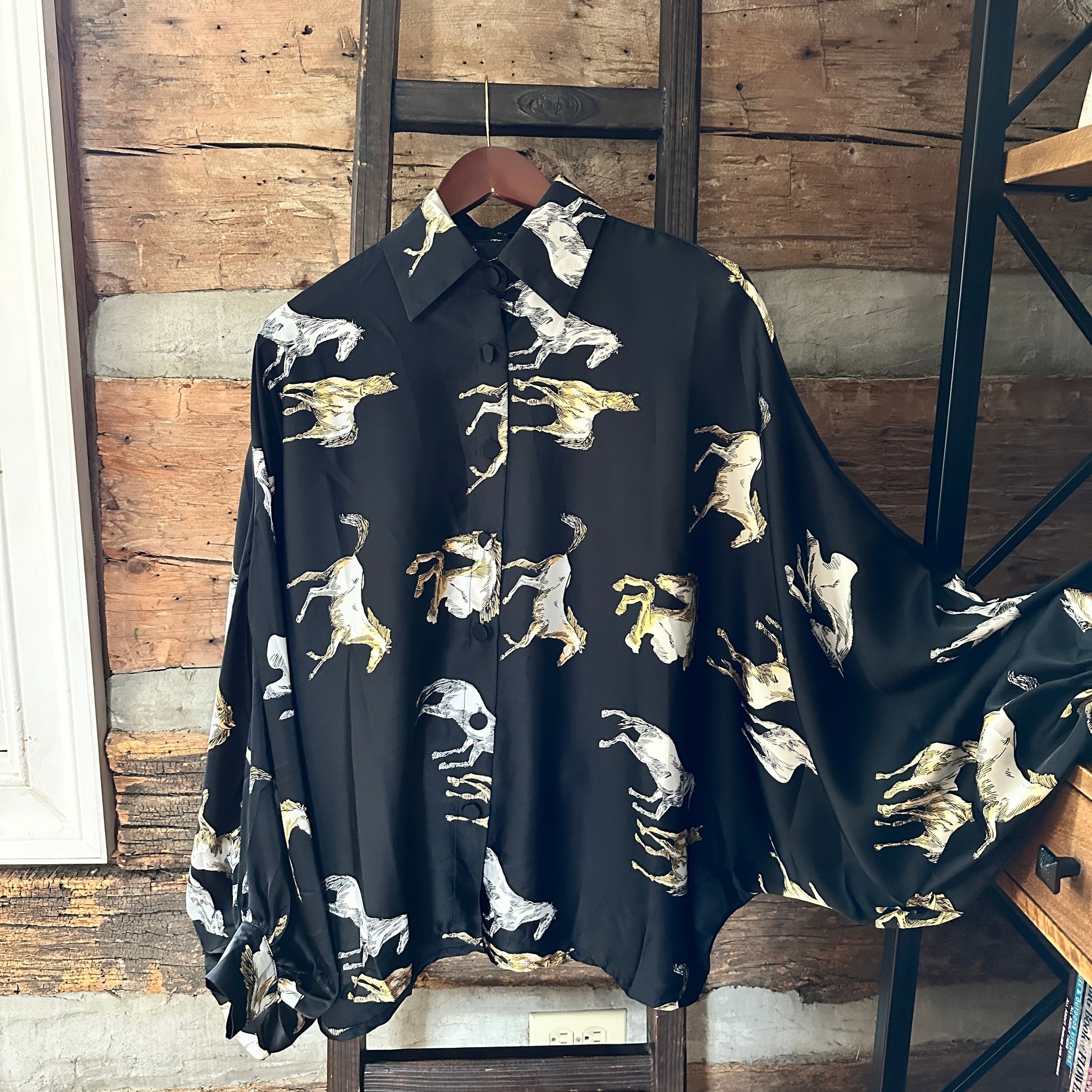 Black shirt with horse print hanging on a wooden rack.