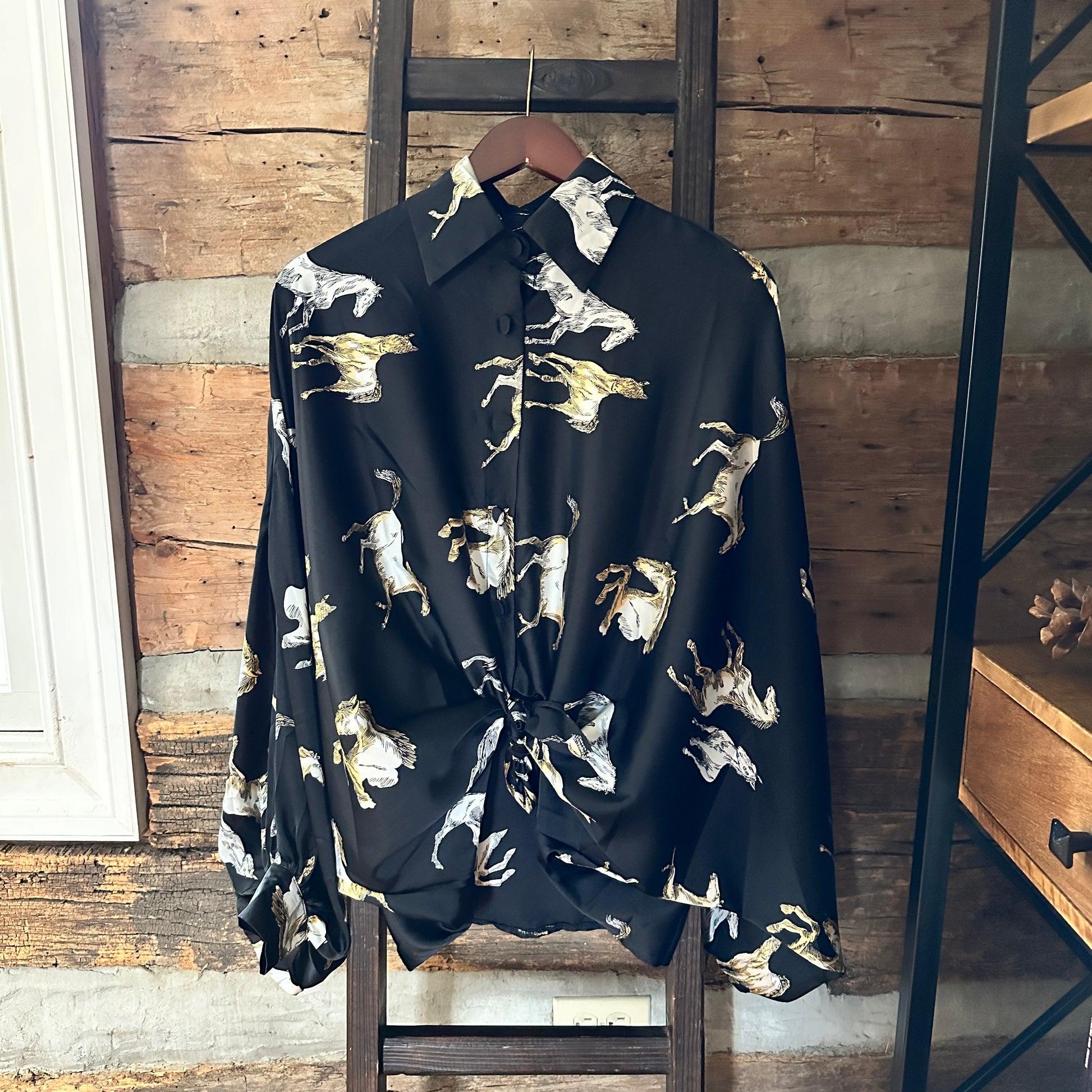 Black shirt with horse print hanging on a wooden ladder.