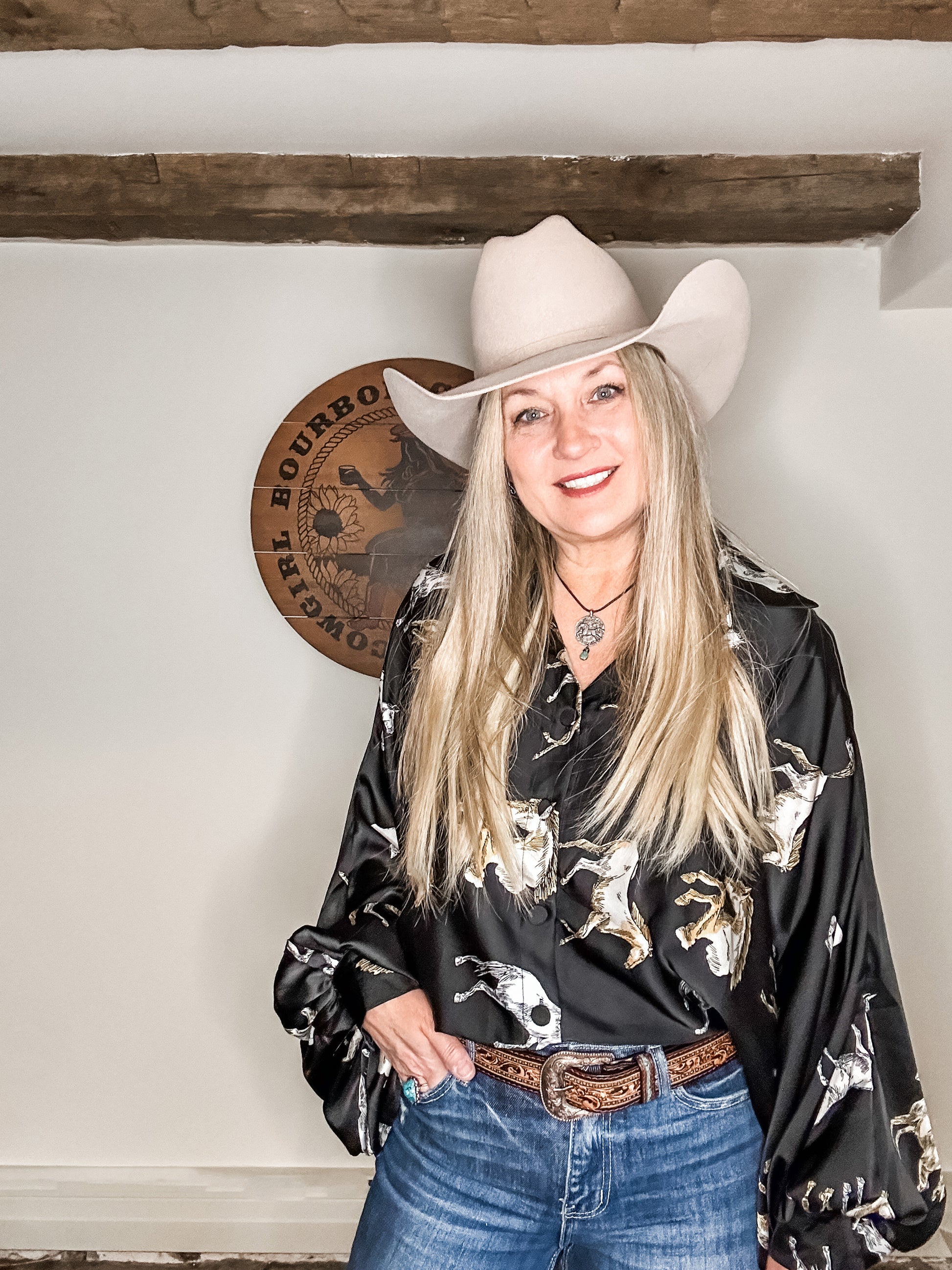 Woman in cowboy hat and shirt with horse print.