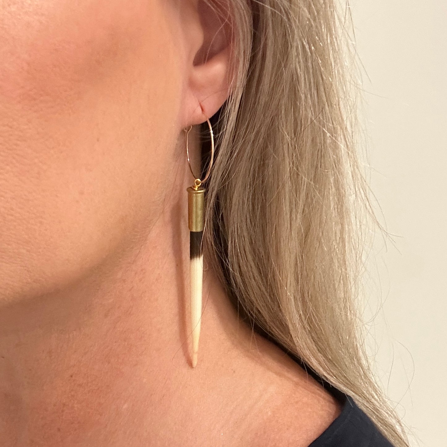 Woman wearing a gold hoop earring with a long, striped pendant.