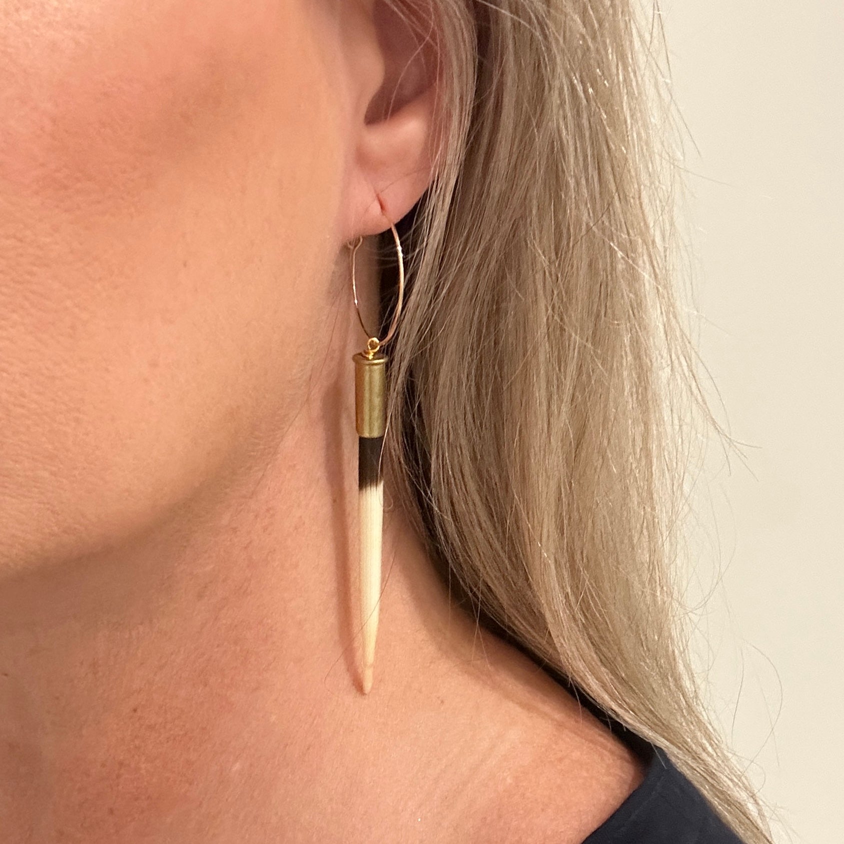 Woman wearing a gold hoop earring with a long, striped pendant.