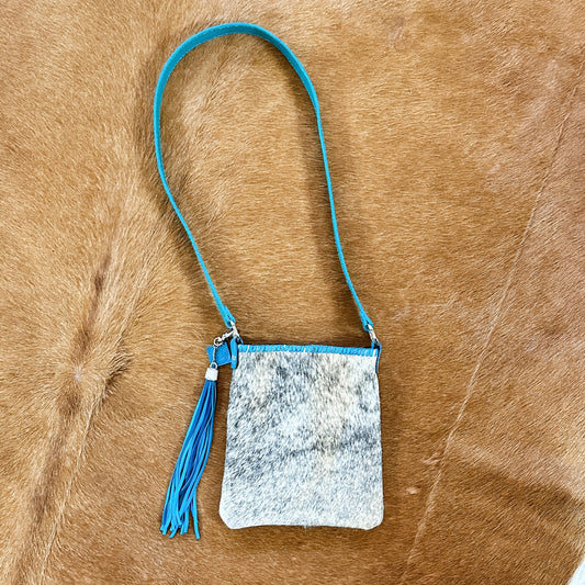Small cowhide crossbody bag with blue strap and tassel.