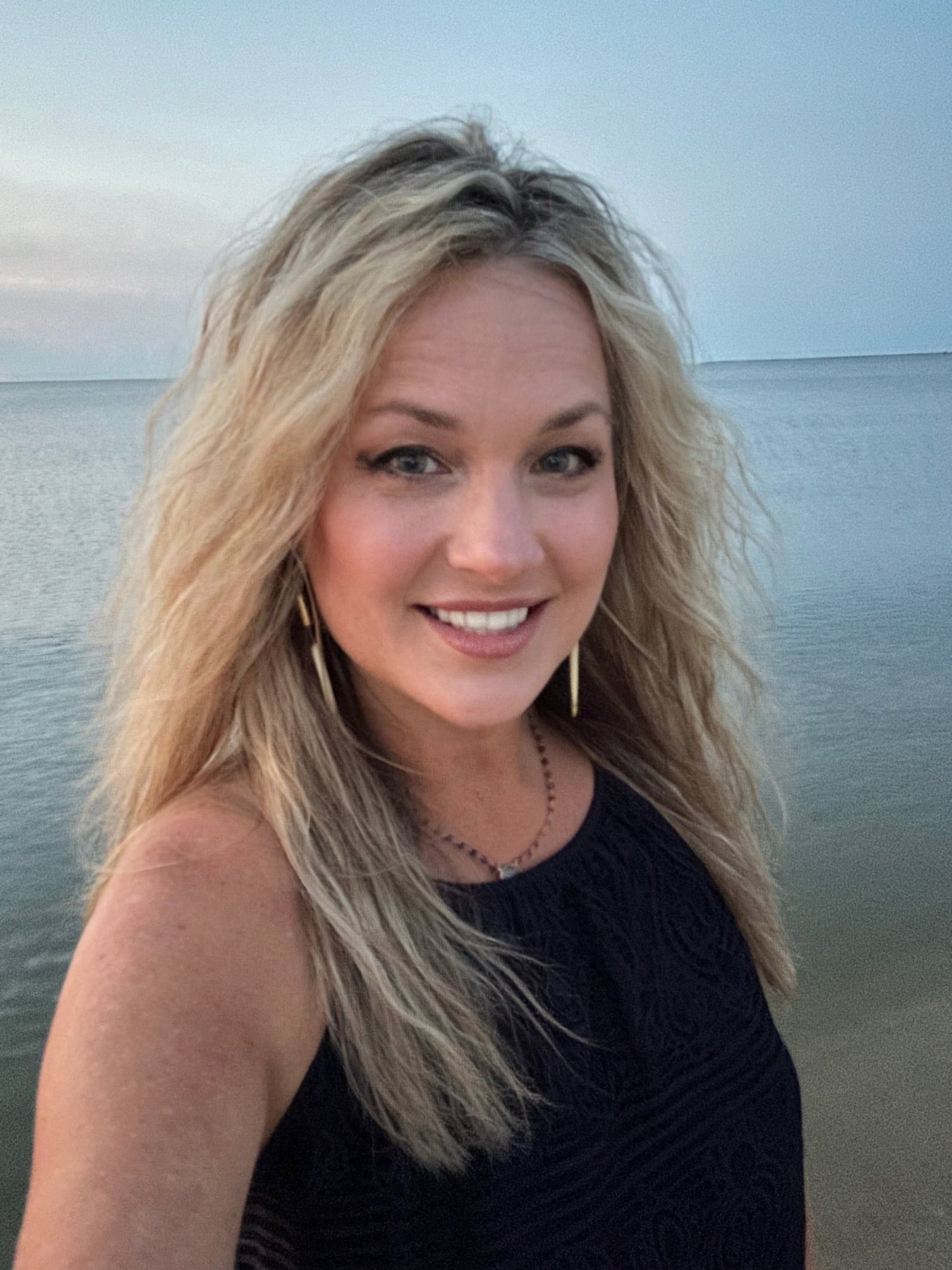 Blonde woman smiling by the water at dusk.