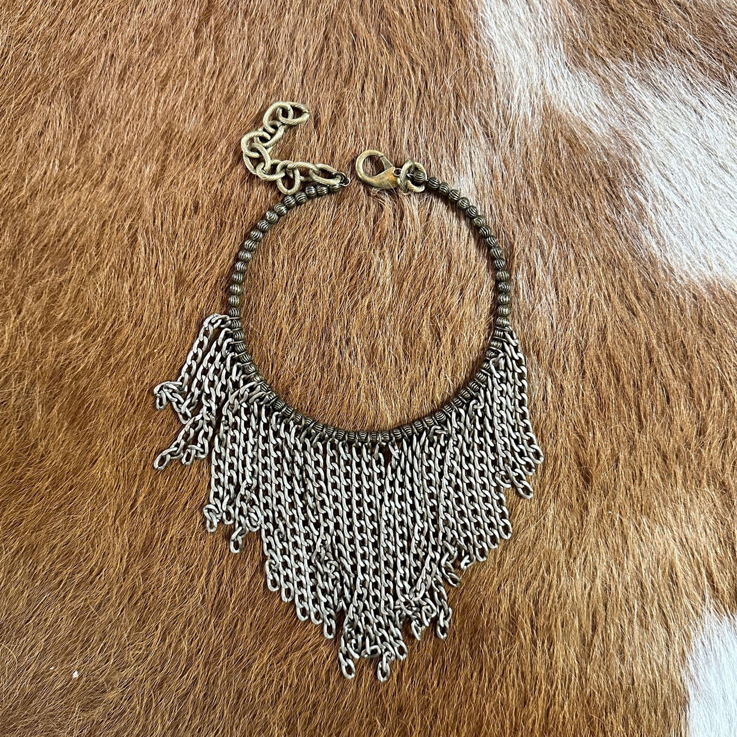 Necklace with chain fringe on brown cowhide.