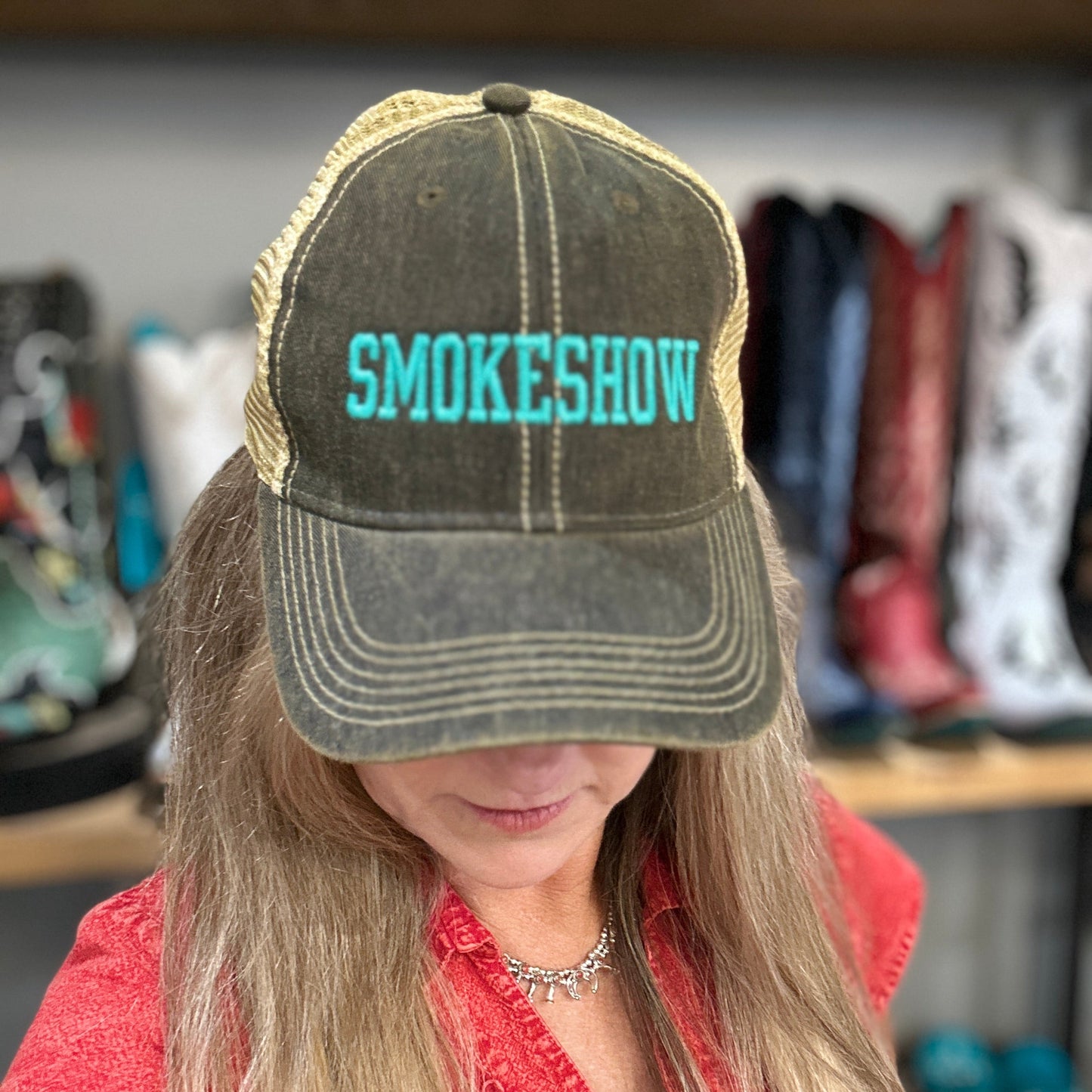 Person wearing a cap with 'SMOKESHOW' text in a store setting with boots and clothing in the background