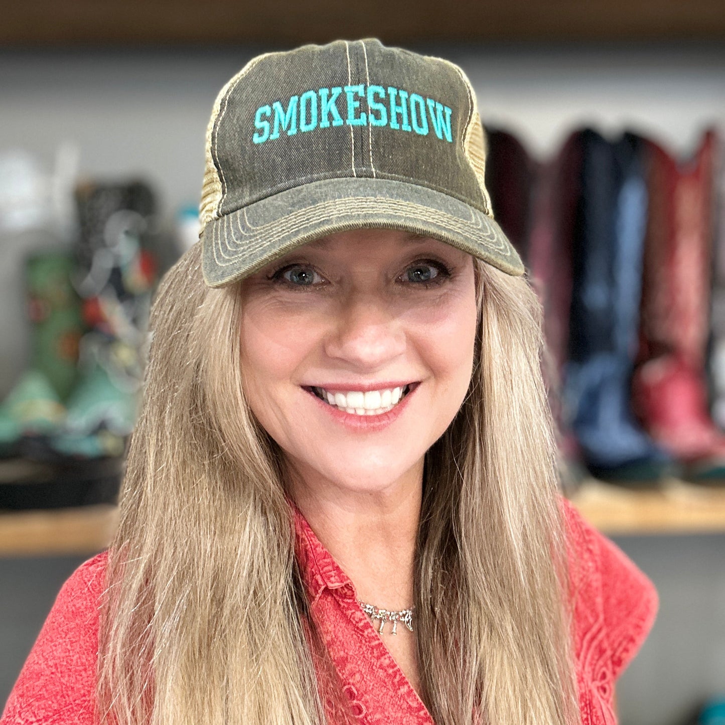 Woman wearing a cap with 'SMOKESHOW' text in a store setting with boots in the background