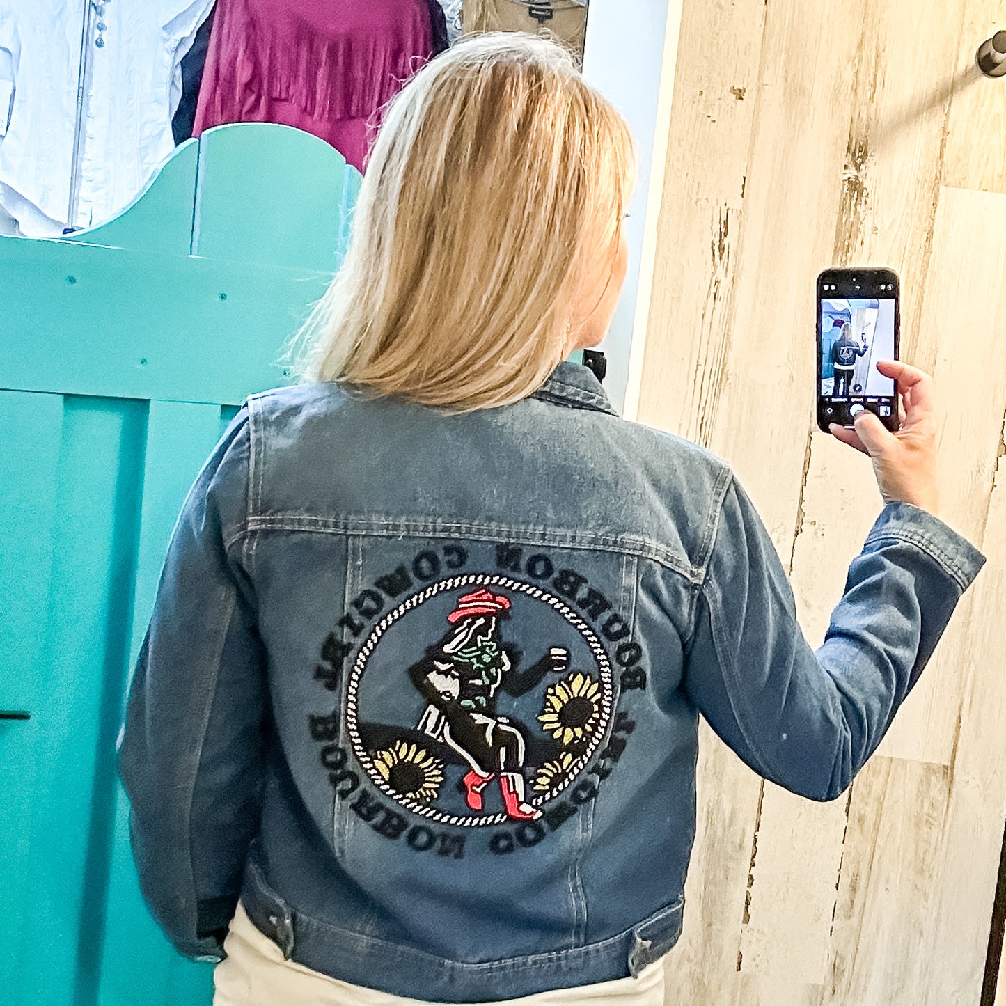 Woman taking a selfie, wearing a denim jacket with a patch.