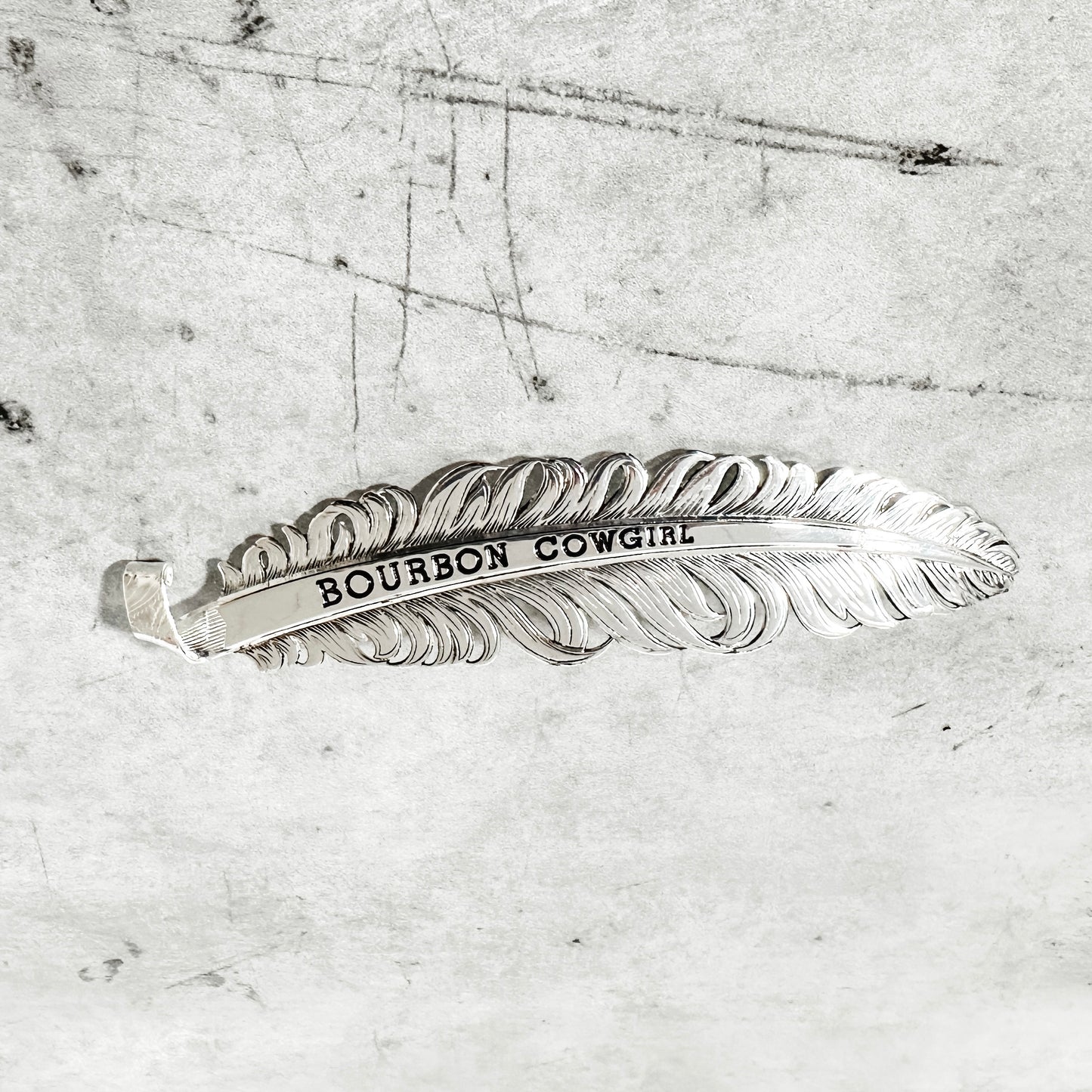 Silver feather with BOURBON COWGIRL engraved.