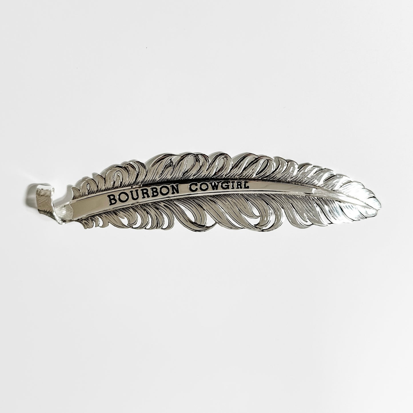 Silver feather-shaped hair clip with Bourbon Cowgirl text.