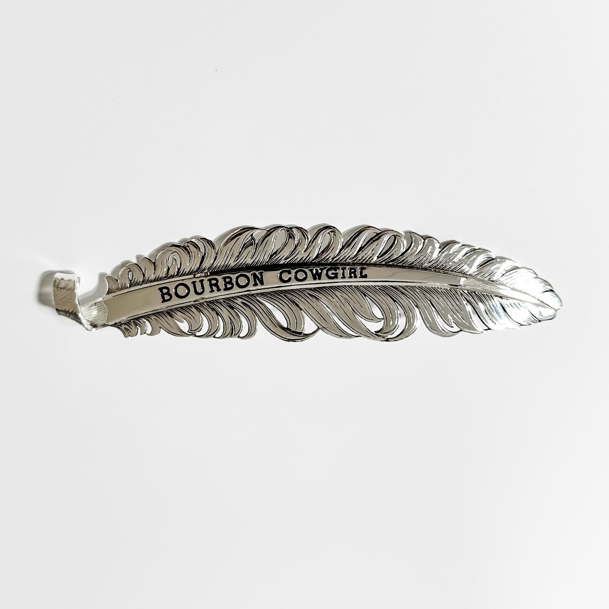 Silver feather-shaped hair clip with Bourbon Cowgirl text.