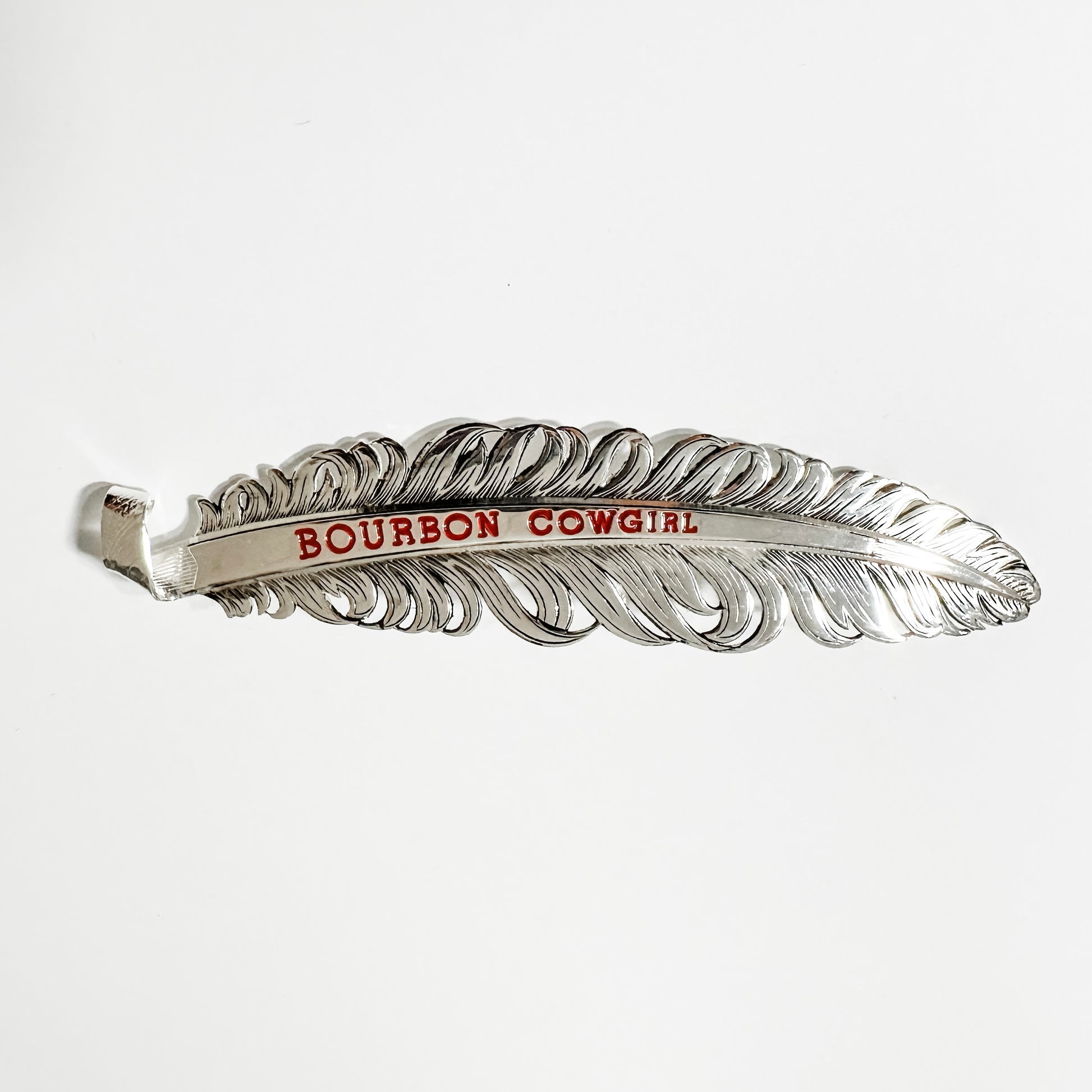 Silver feather-shaped bottle opener with Bourbon Cowgirl text.