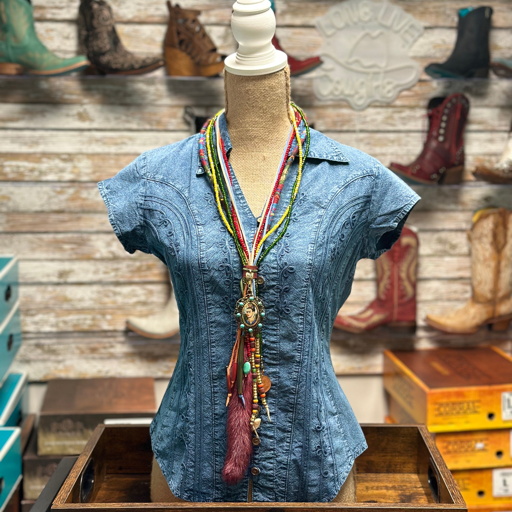 Blue denim shirt on a mannequin with a beaded necklace.