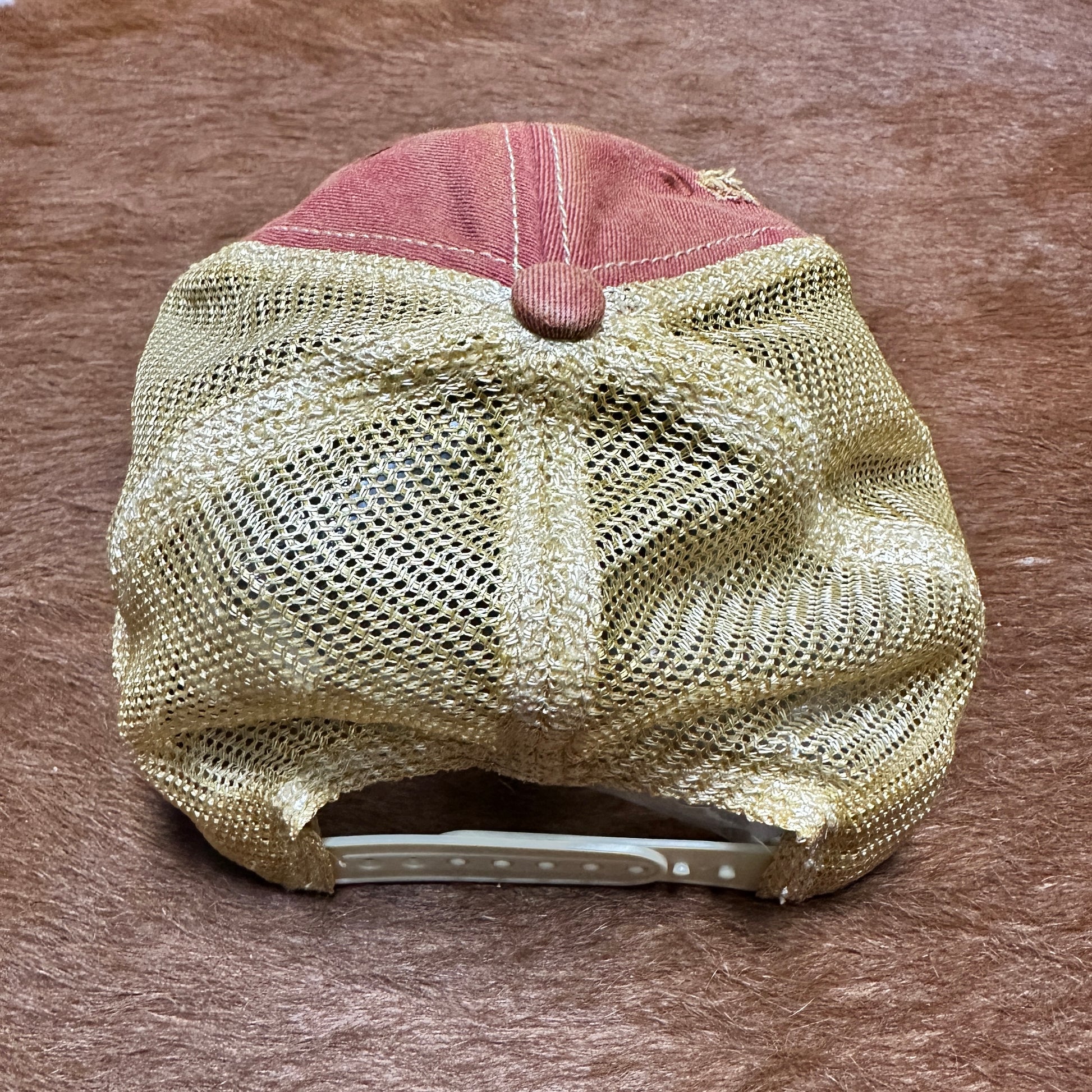 Red and tan trucker hat on brown surface.