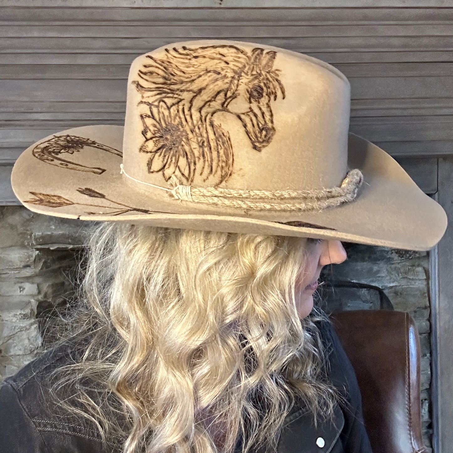 Woman wearing a beige cowboy hat with horse and flower design.