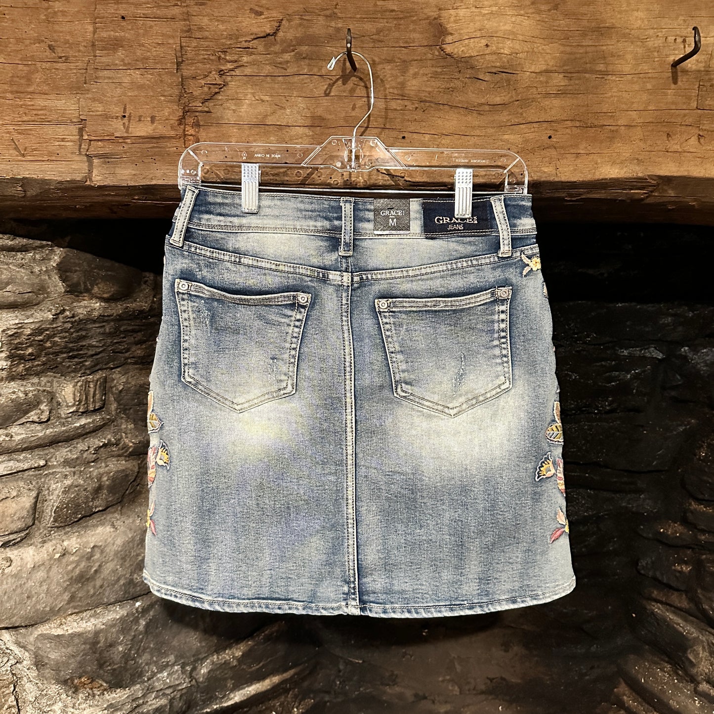 Denim skirt with floral embroidery hanging on a hanger.