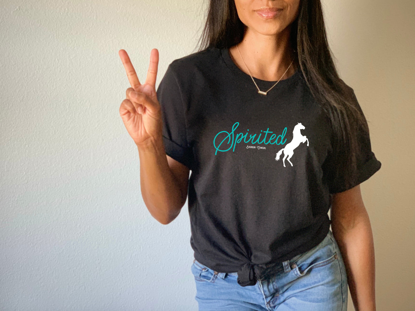 Woman in black tee with horse logo, making peace sign.