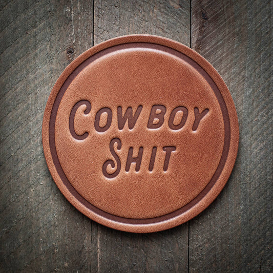 Brown leather coaster with Cowboy Shit text.