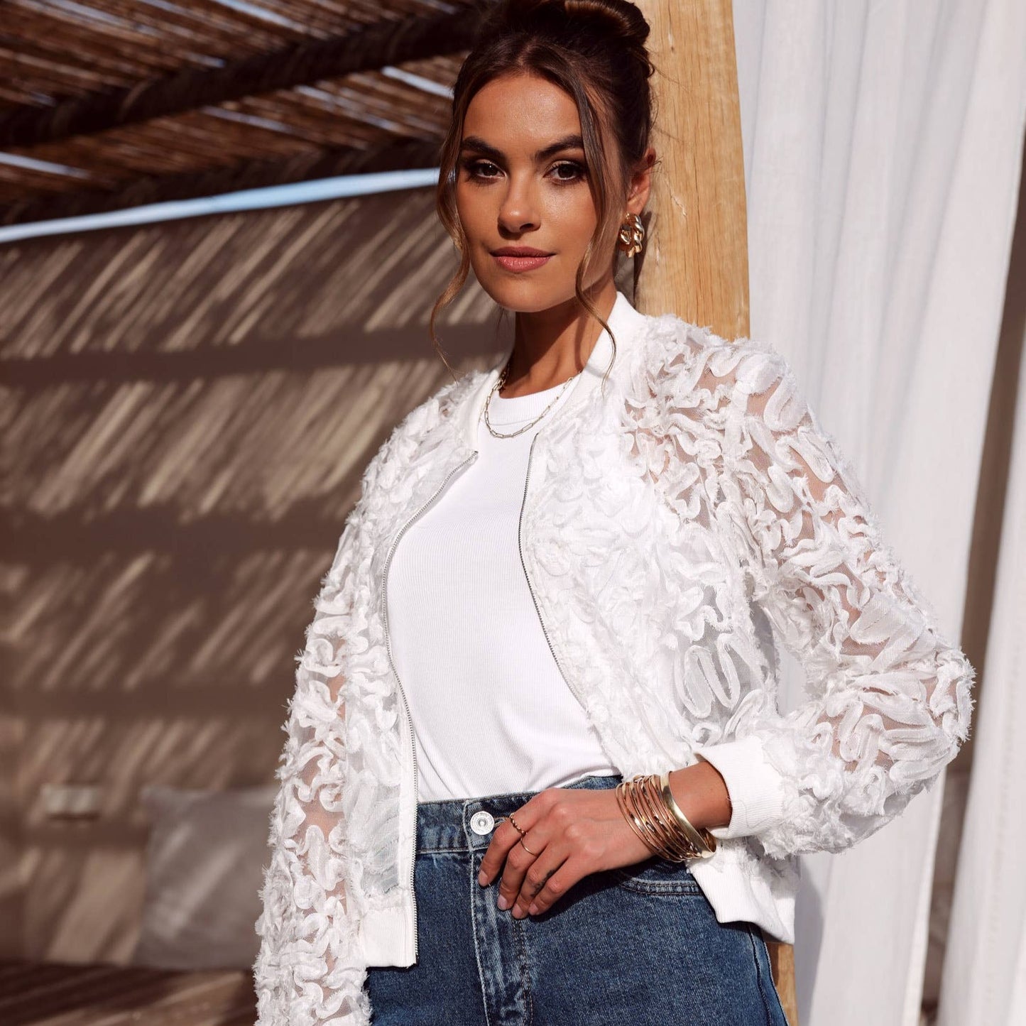 Woman wearing a white lace jacket and jeans.