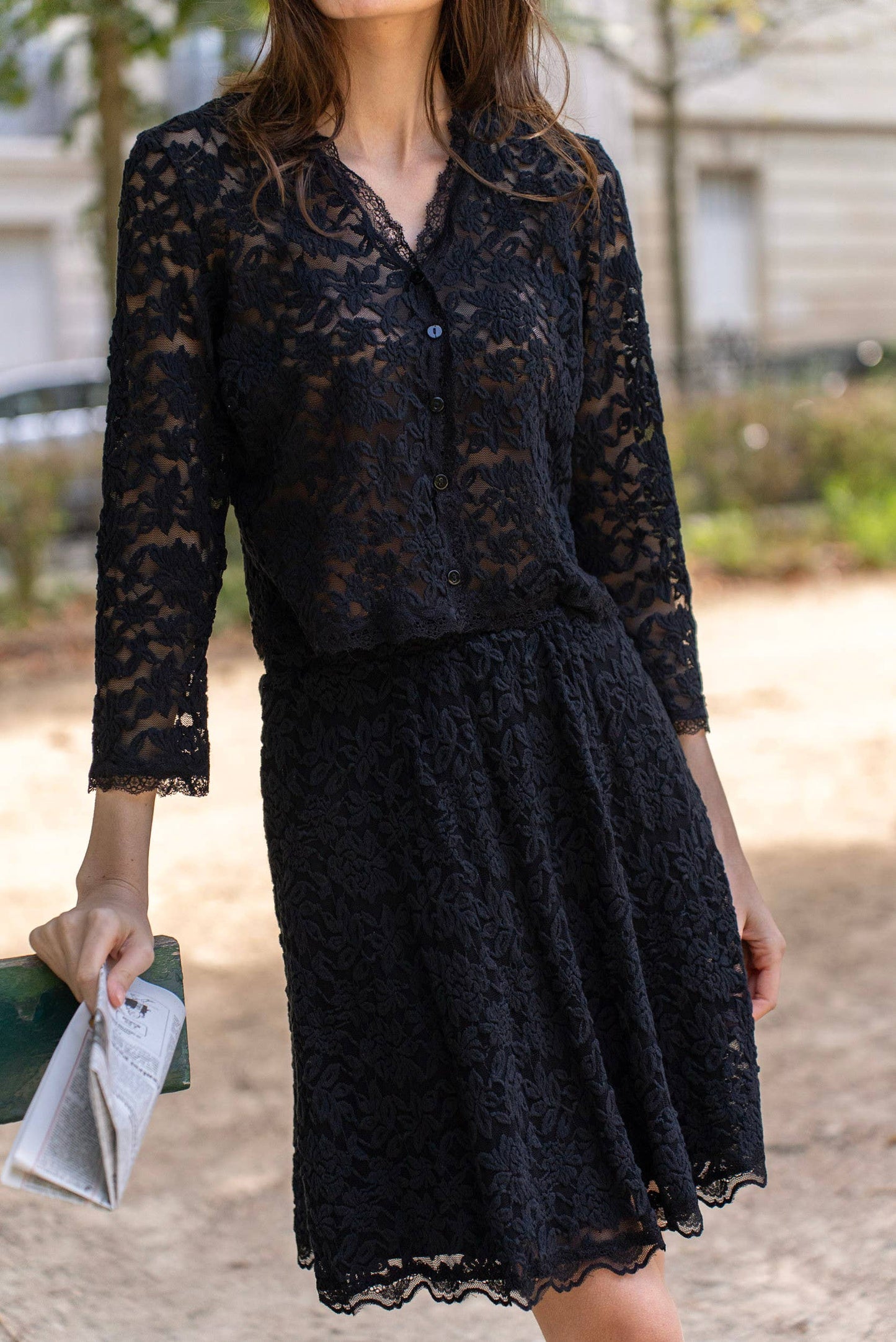 Woman in black lace dress holding a newspaper.