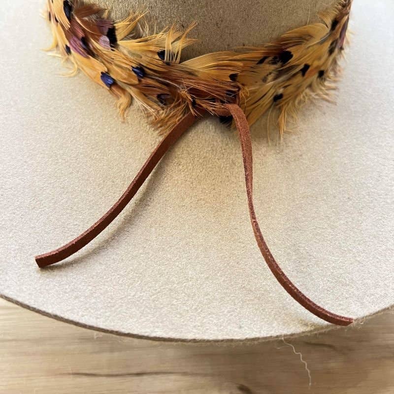 Tan hat with feather and leather details.