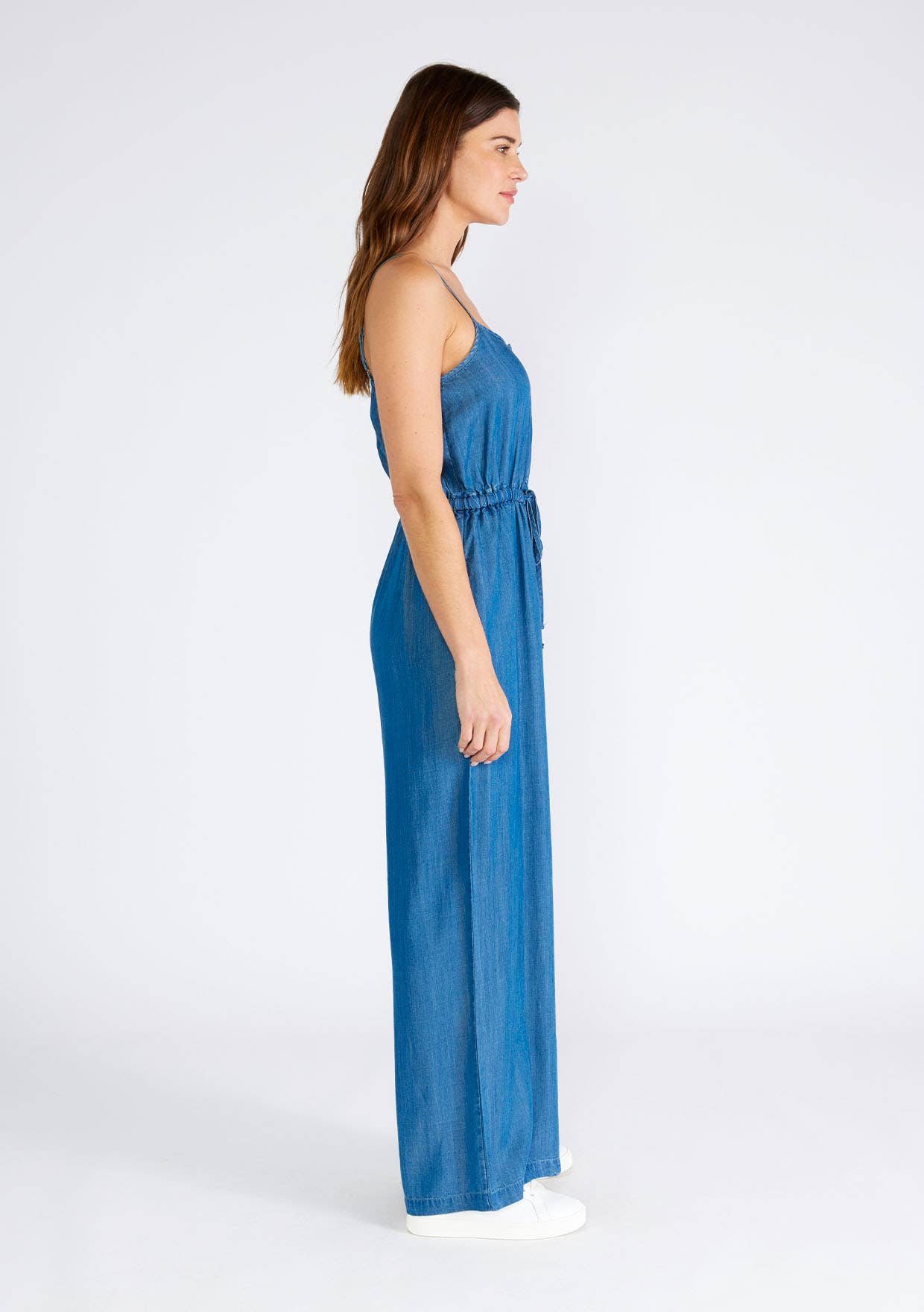 Woman in a blue denim jumpsuit, standing sideways.