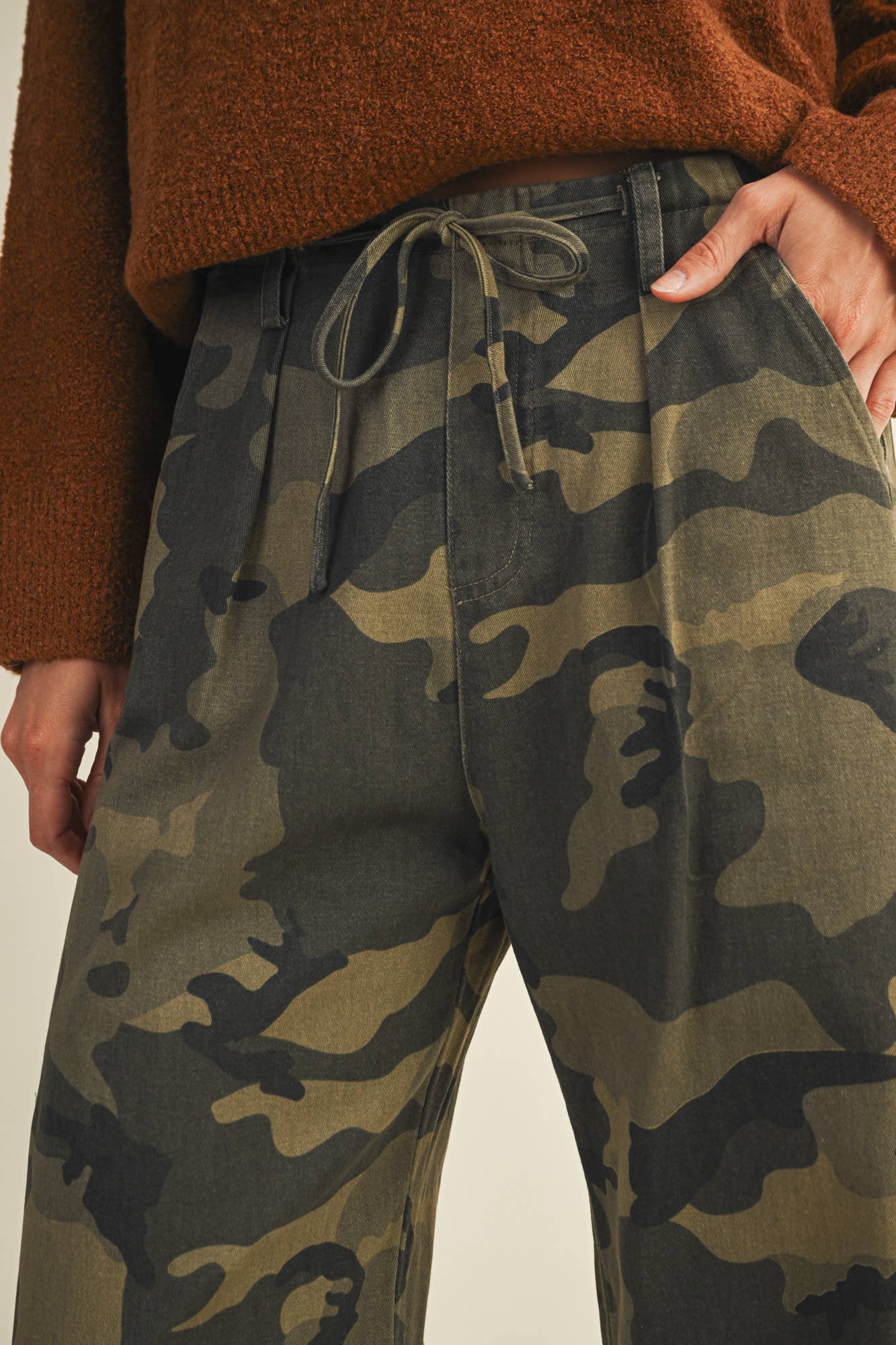 Woman wearing camouflage pants and brown sweater.