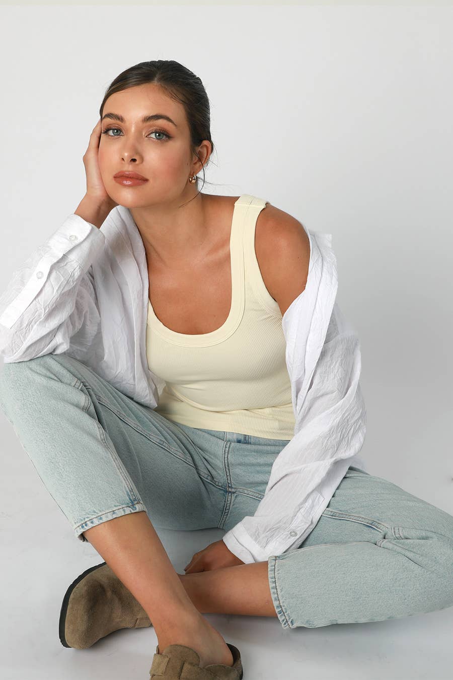 Woman in tank top, jeans, and shirt, seated.