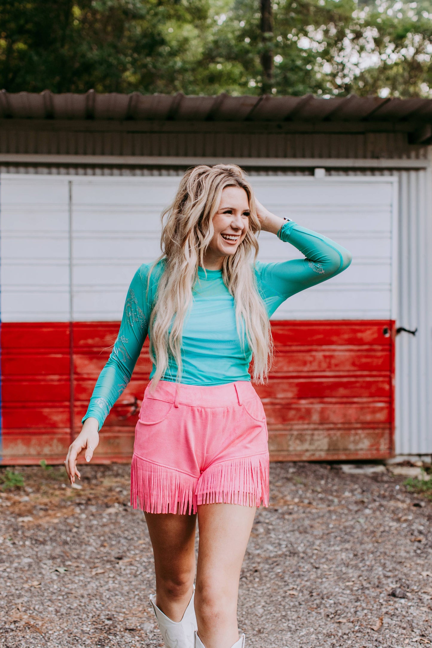 Woman in turquoise top and pink fringed shorts.