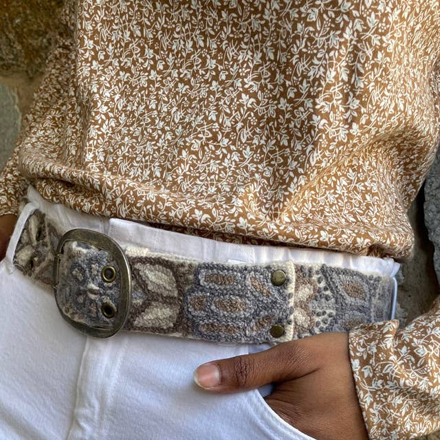 Woman wearing floral top, patterned belt, and white pants.