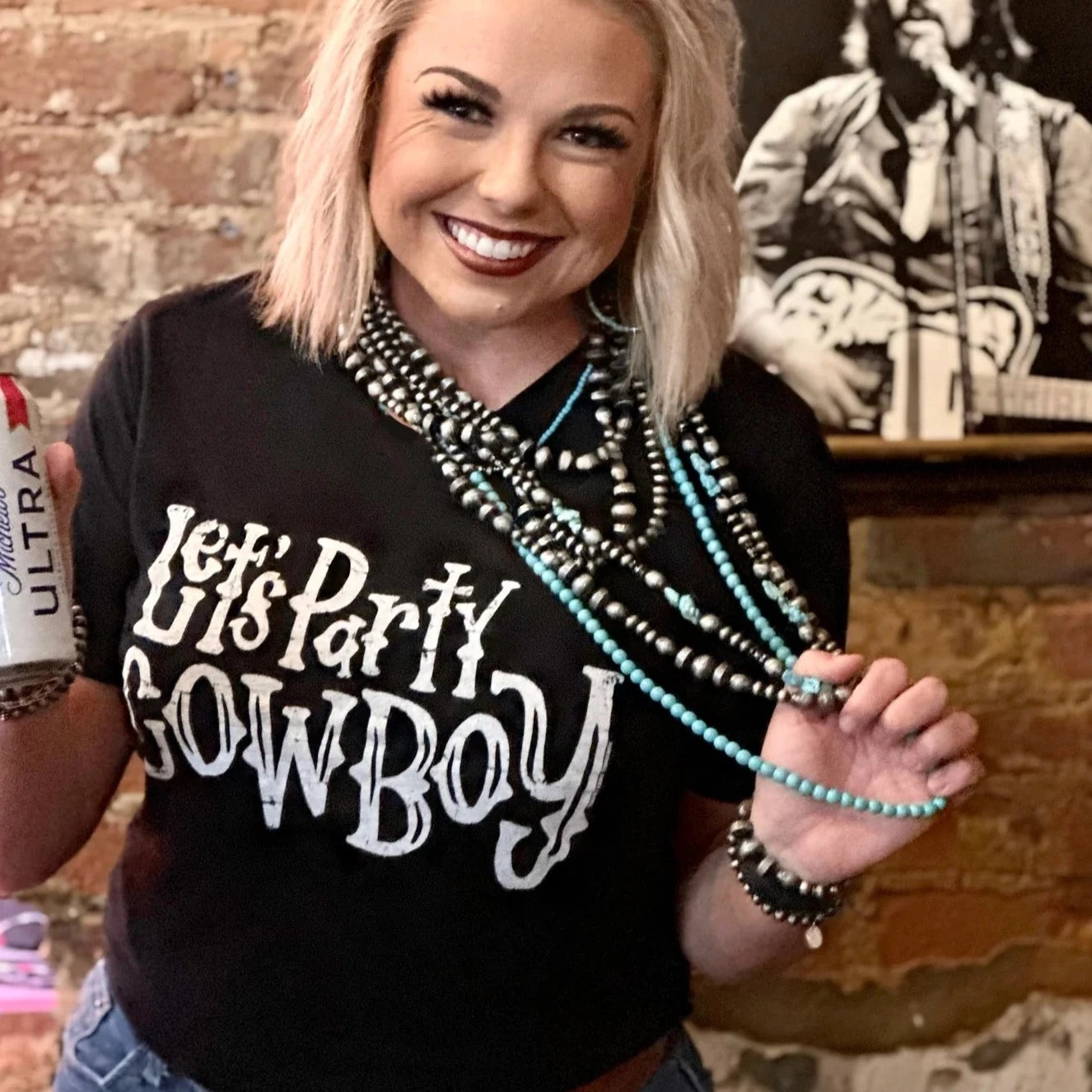 Woman in Let's Party Cowboy shirt holding beer and jewelry