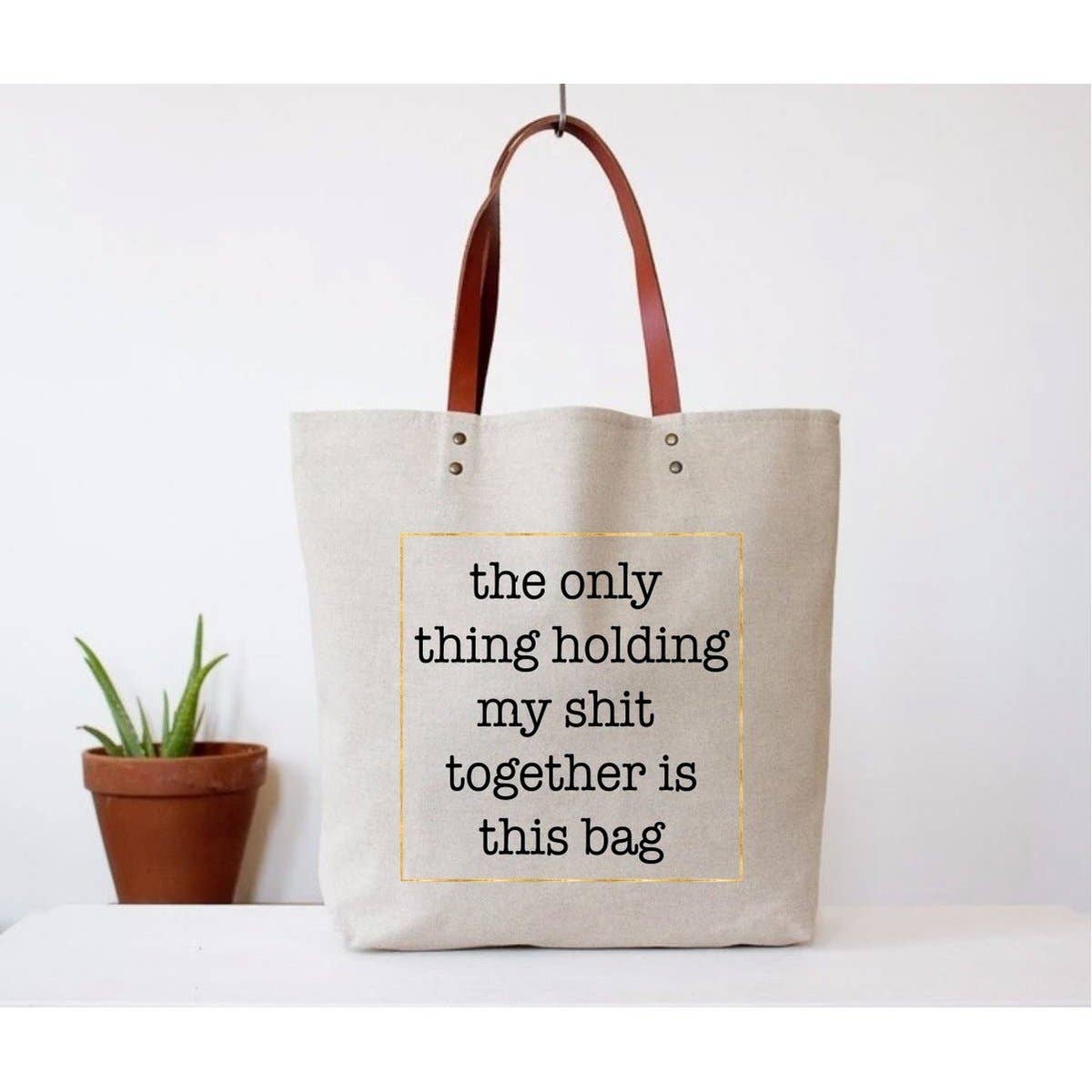 Beige tote bag with leather handles and text.