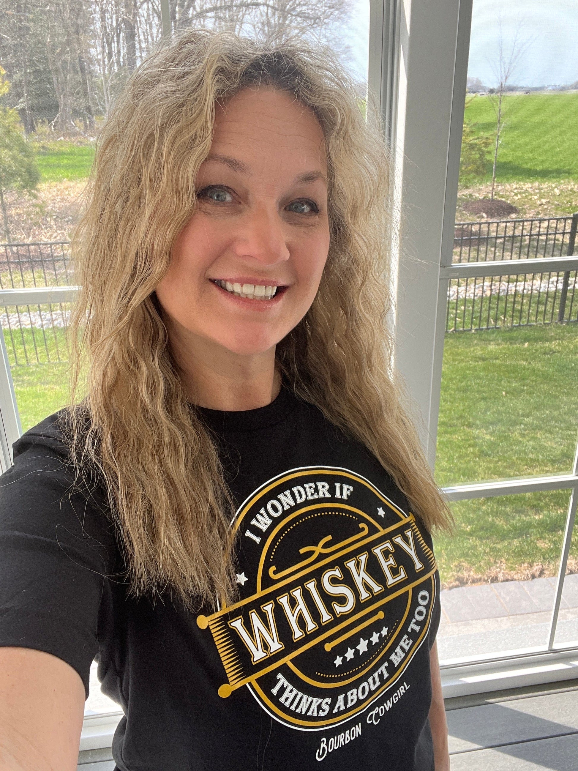 Woman with long blonde hair smiling, wearing a black t-shirt.