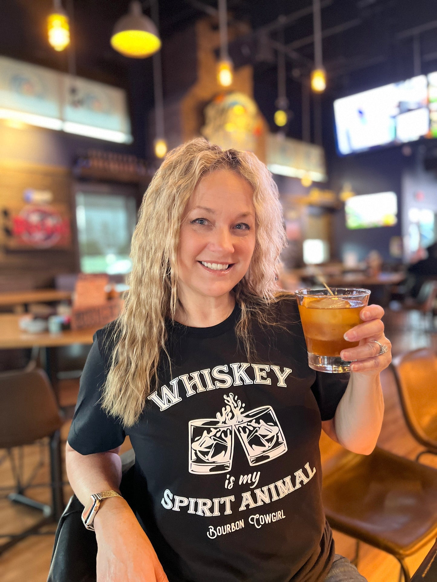 Woman smiling, holding a cocktail, wearing a Whiskey is my spirit animal...
