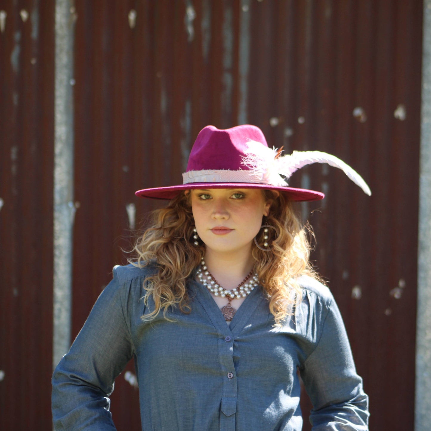 Woman wearing a magenta hat with a feather and pearl necklace.
