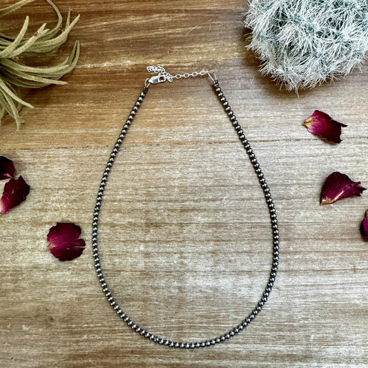 Silver bead necklace on wood surface with rose petals
