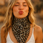Woman with blonde hair and leopard print scarf blowing a kiss.